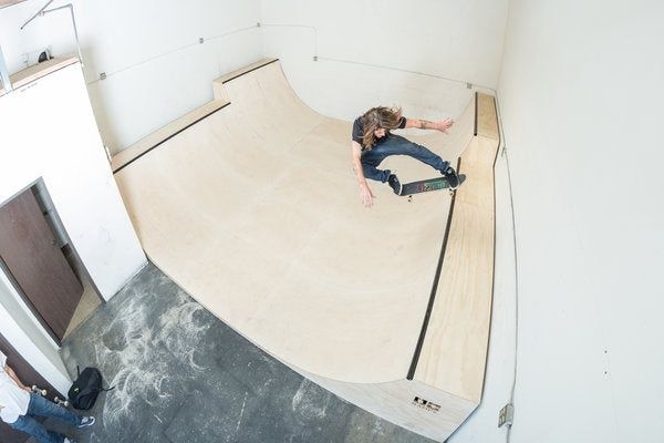 Skateboardåkare gör ett trick i en inomhusramp av trä